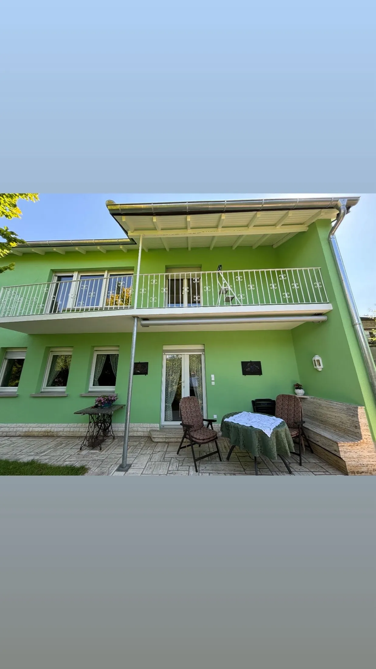 Hochformataufnahme der fertig grün gestrichenen Gartenfassade mit Balkon und Markise