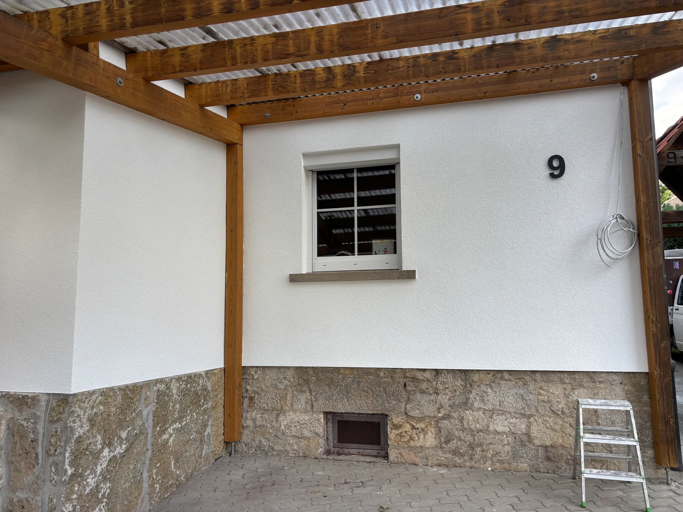 Frisch gestrichene Hauswand mit Fenster unter einer Holzpergola nach Abschluss der Malerarbeiten