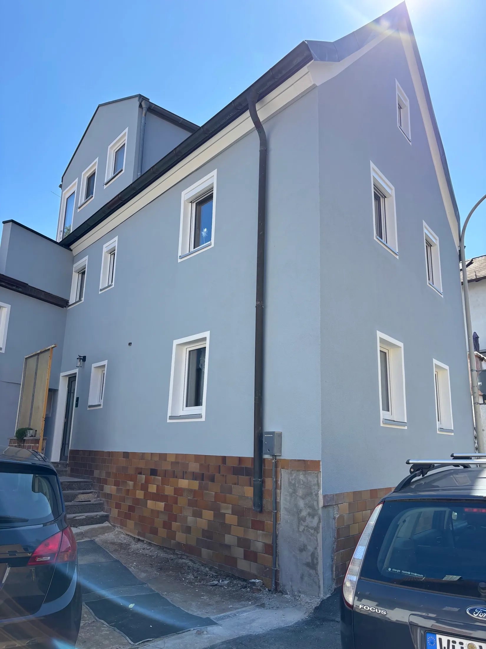 Dreigeschossiges Wohnhaus mit blaugrauer Fassade, weißen Faschen und Klinkersockel