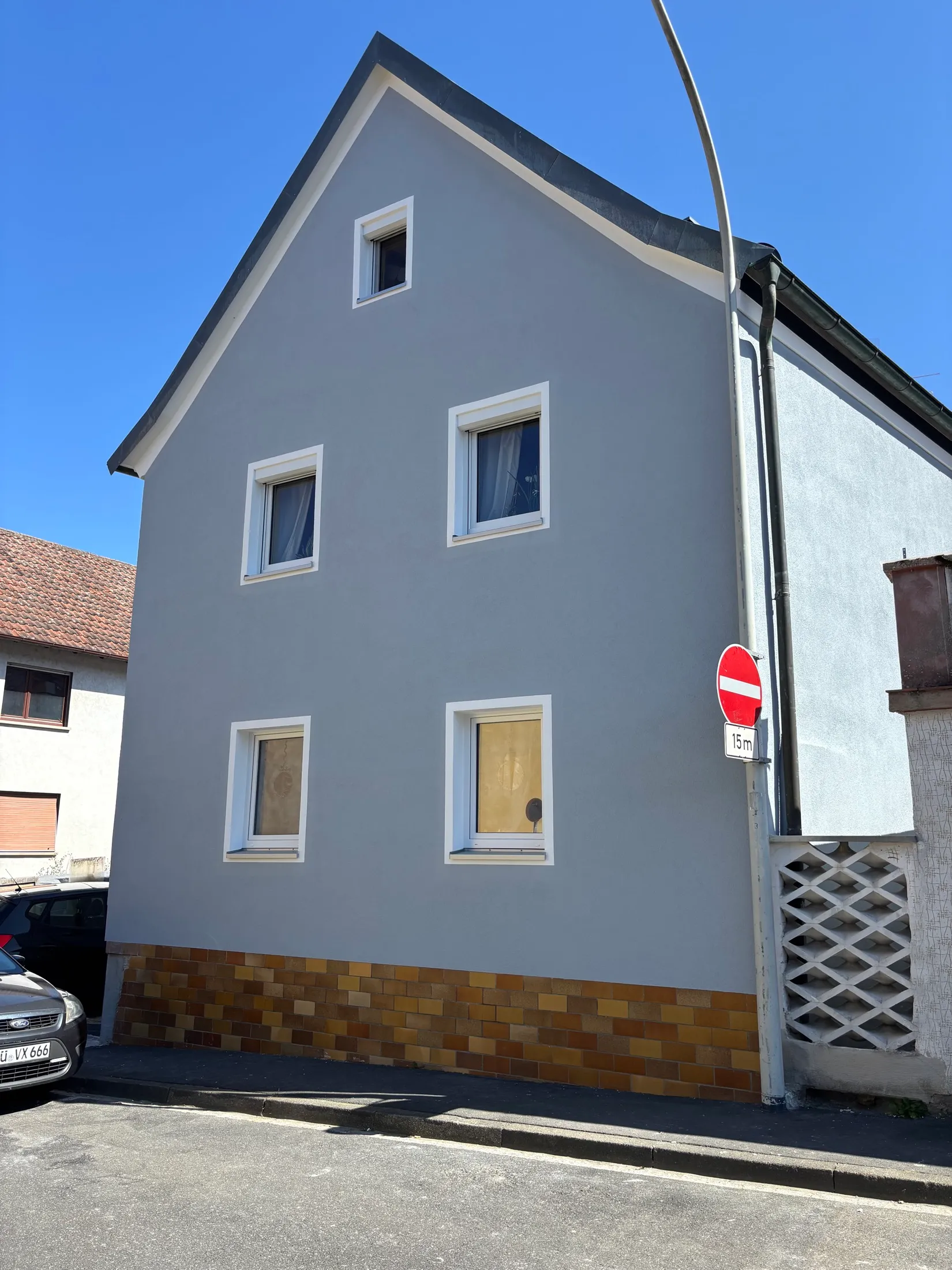 Frontansicht der fertig gestrichenen blaugrauen Giebelfassade mit weißen Fensterlaibungen und Klinkersockel