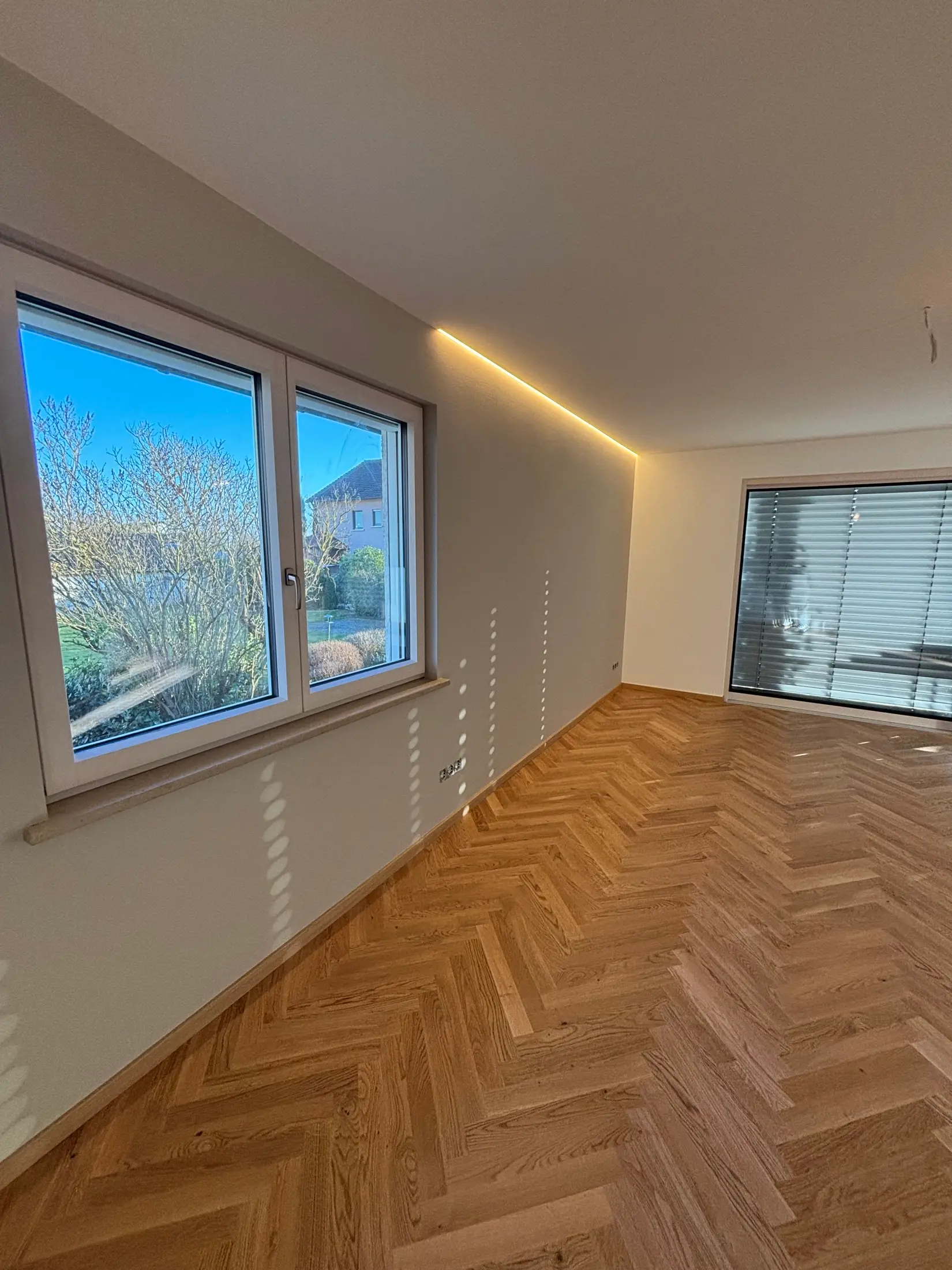 Renoviertes Zimmer mit glatten weißen Wänden, LED-Lichtvoute und Fischgrätparkett