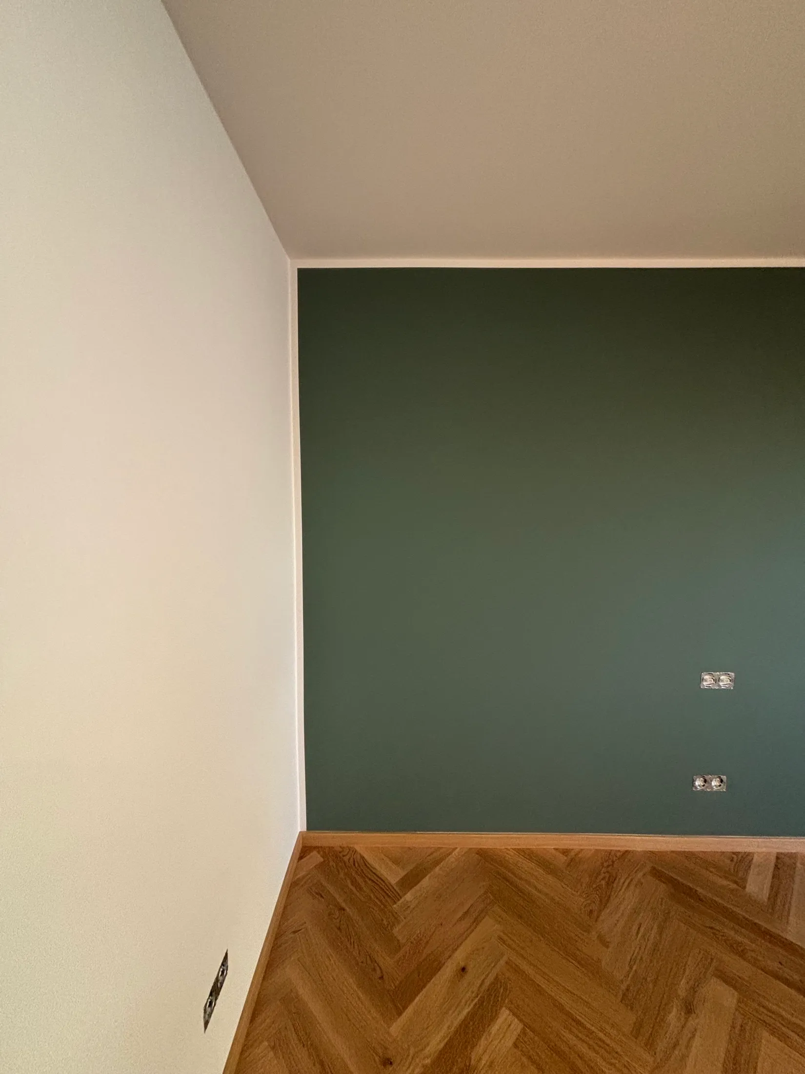 Dunkelgrüne Akzentwand neben weißer Wand über neuem Fischgrätparkett