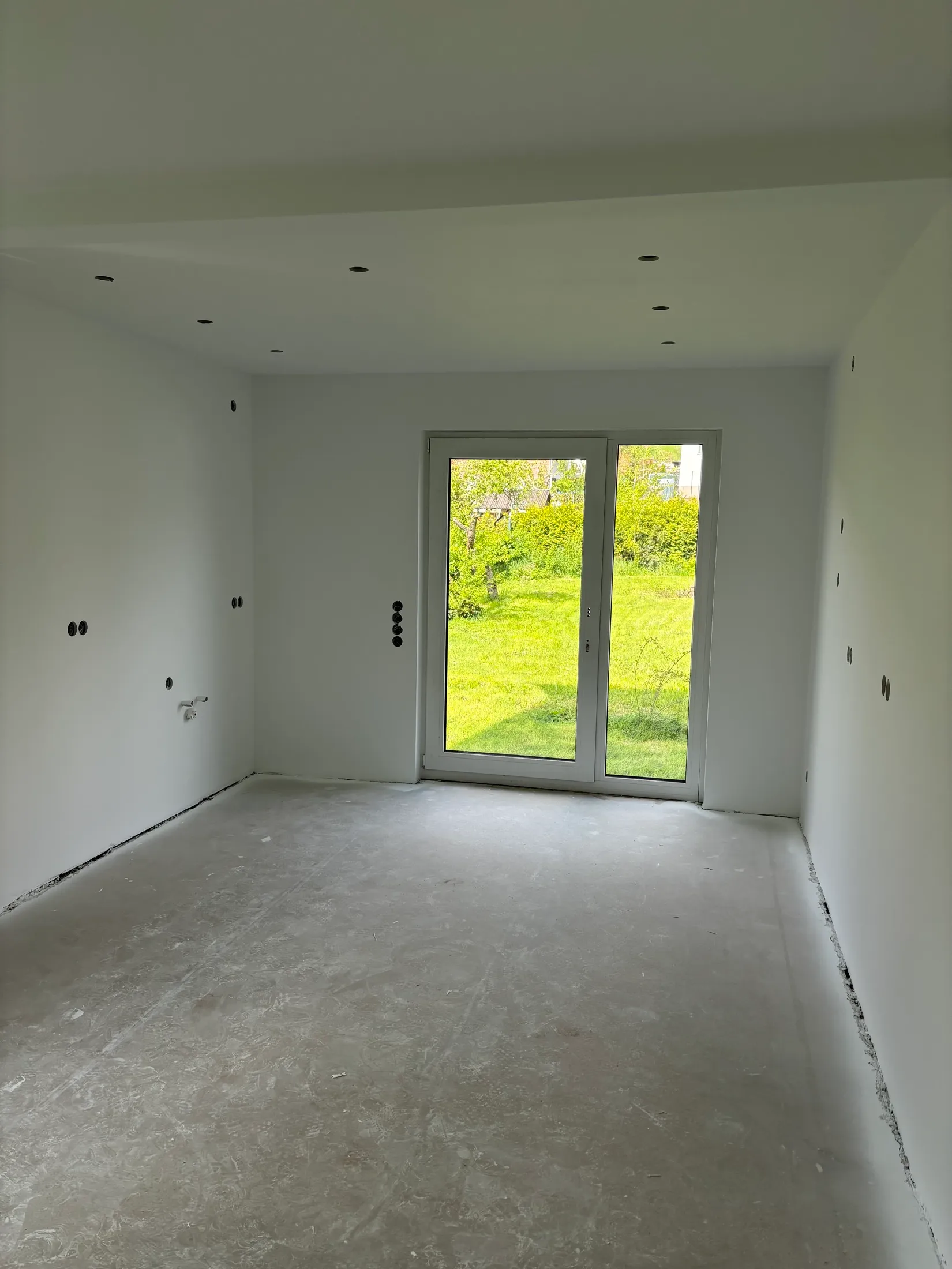 Großer, frisch weiß gestrichener Wohnraum mit Deckenspots und dreiteiligem Fenster