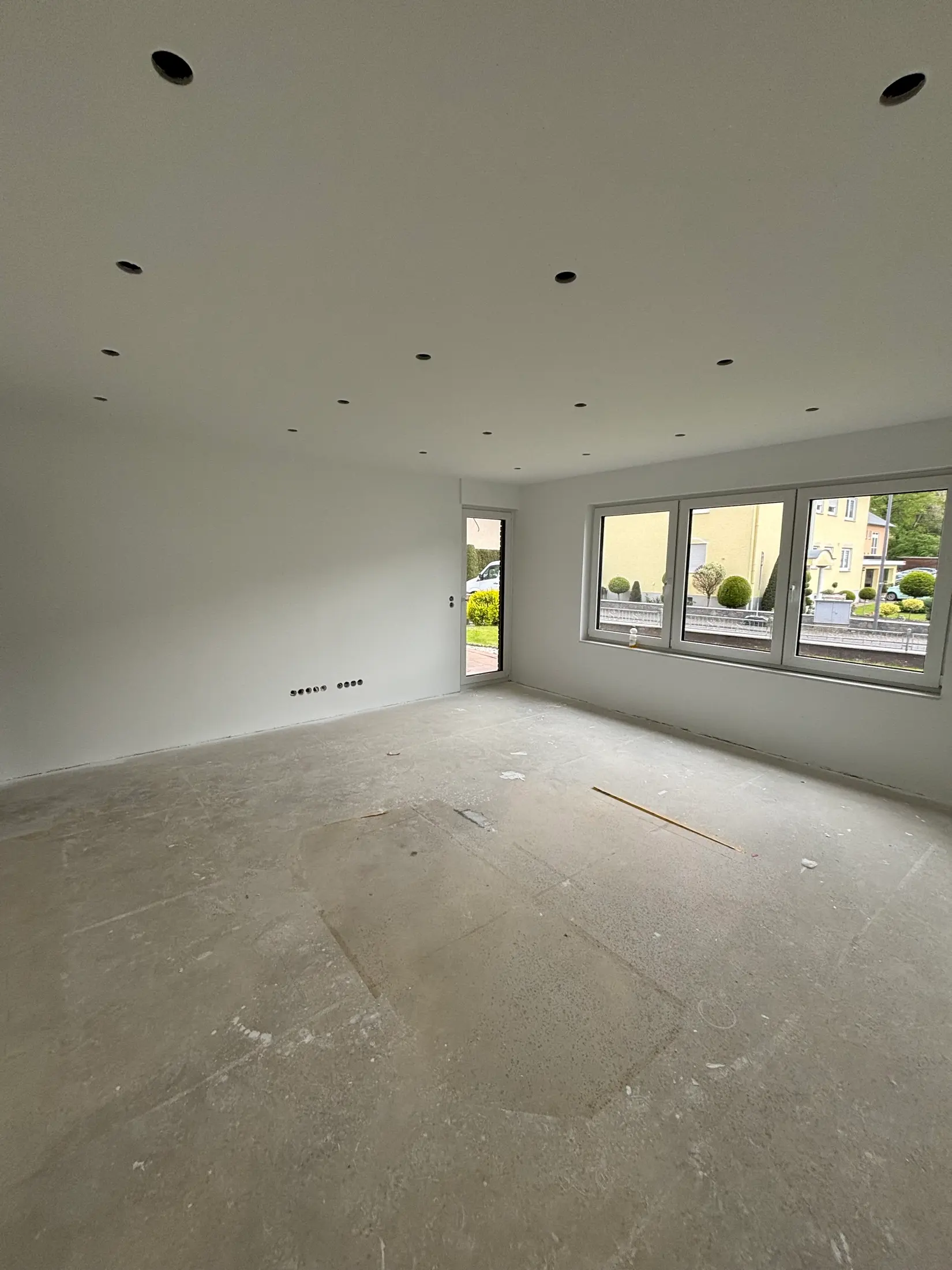 Renovierter Raum mit frisch gestrichenen Wänden, Deckenspots und Terrassentür zum Garten